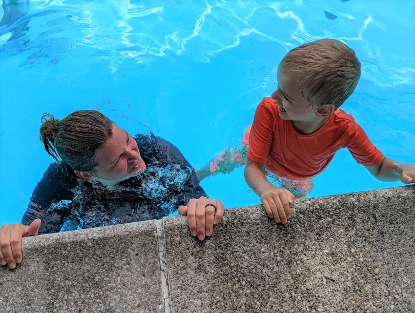 Swim instructor and student holding wall in the water and smiling at eachother