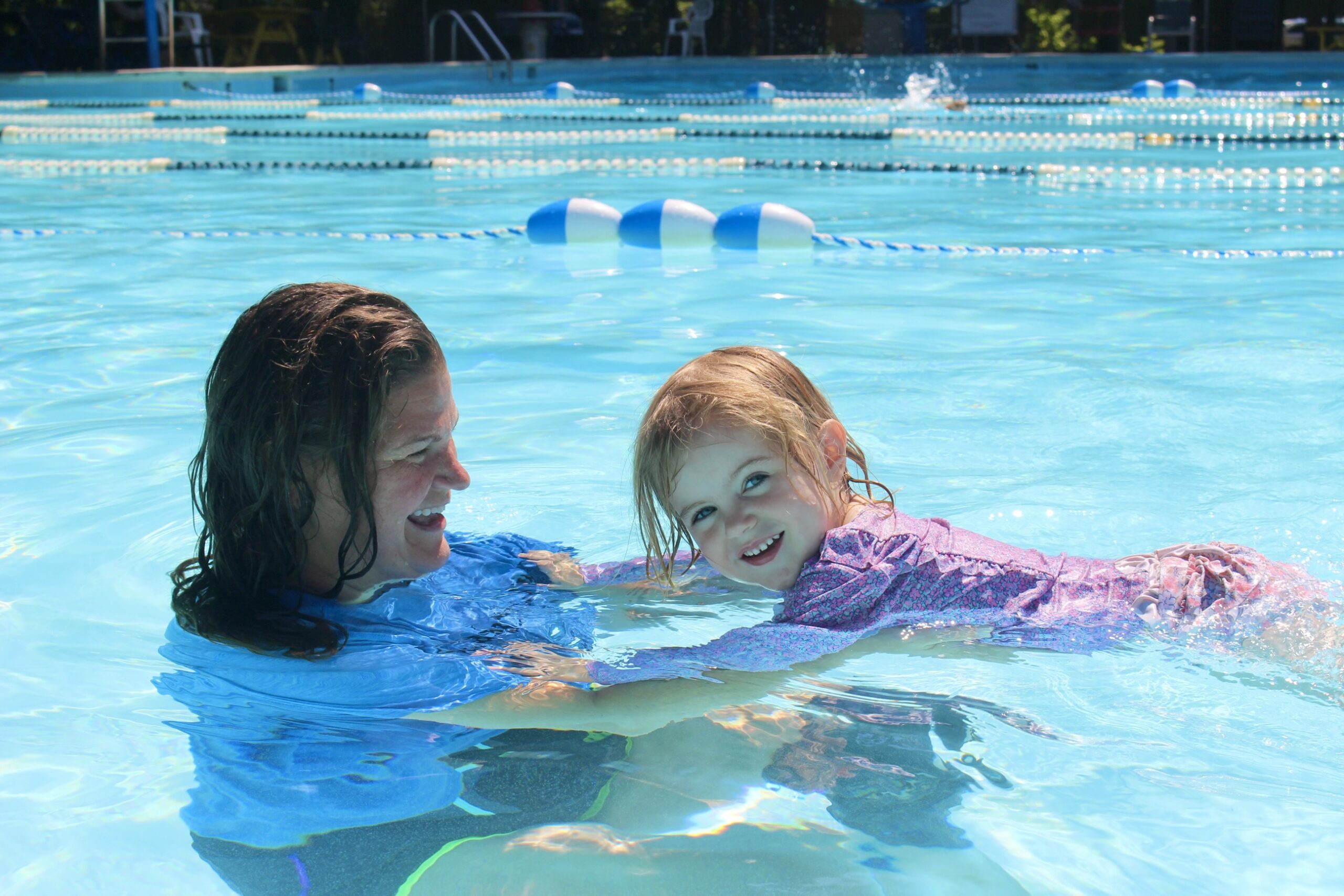 traditional swim class of instructor in water with young girl looking at the camera as she floats and swims with assistance